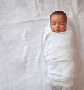 A one month old baby sleeping and swaddled in white cloth lying in white cloth background