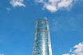 One multi-storey high mirrored shiny skyscraper against a blue sky with clouds. Bottom view