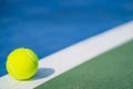 One new tennis ball on white diagonal line in blue and green hard court with light from left Royalty Free Stock Photo