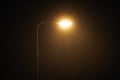 One night lamppost shines with faint mysterious yellow light through evening fog, copy space