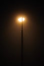 One night lamppost shines with faint mysterious yellow light through evening fog