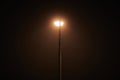 One night lamppost shines with faint mysterious yellow light through evening fog