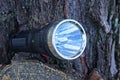 one old black electric flashlight lies on a pine stump