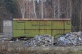 One old green iron container in rust stands on the street near heaps of garbage