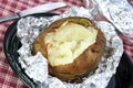 One open baked potato on aluminum foil, unwrapped.