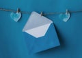 One opened blue envelope hanging on rope isolated blue background with two blue hearts on sides. Write a letter to a friend.