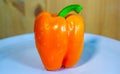 One orange bellpepper on a plate with wooden background