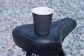one paper black paper cup with coffee stands on a leather bicycle seat