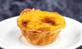 One Pastel de nata or Portuguese egg tart on a white plate. Pastel de Belm is a small pie with a crispy puff pastry