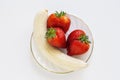 One peeled banana and three ripe strawberries in a plate, on a white background Royalty Free Stock Photo