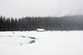 One person dressed in red in a winter landscape. Frozen lake, wooden house and a forest under the snow. Banff National Park, Alber Royalty Free Stock Photo