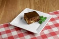 One piece of chocolate brownie cake served on a square plate over wooden background with red plaid tablecloth Royalty Free Stock Photo