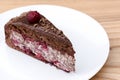 One piece of chocolate cake with vanilla cream and cherry topping served on white plate over light wooden background. Royalty Free Stock Photo