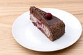 One piece of chocolate cake with vanilla cream and cherry topping served on white plate over light wooden background. Royalty Free Stock Photo