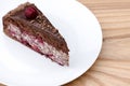 One piece of chocolate cake with vanilla cream and cherry topping served on white plate over light wooden background. Royalty Free Stock Photo