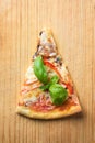 One piece of Italian pizza with tomatoes mushrooms bacon and cheese and basil leaves on wooden background cutting board Royalty Free Stock Photo