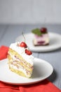 One piece of vanilla cherry cake on a white plate over light wooden background. Delicious sweet dessert close up. Royalty Free Stock Photo