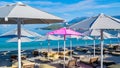 One pink open beach umbrella among the rest of grays. Large beach umbrellas over sun loungers on pebble beach