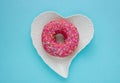 One pink sweet doughnut sits on a white heart-shaped plate on a blue background Royalty Free Stock Photo