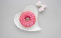 One pink sweet doughnut sits on a white heart shaped plate on a gray background Royalty Free Stock Photo