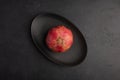One pomegranate in the peel served in black oval plate