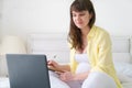 One pregnant european woman working from her home while she is sitting on a white bed at day time Royalty Free Stock Photo