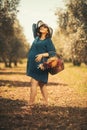 One pregnant woman with a blue dress white hat and a basketfull dry flowers in an olive field with shallow depth of field Royalty Free Stock Photo