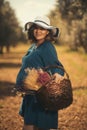 One pregnant woman with a blue dress white hat and a basketfull dry flowers in an olive field with shallow depth of field Royalty Free Stock Photo