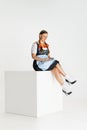 One pretty woman, waitress in traditional Austrian or Bavarian costume sitting on huge box isolated over white Royalty Free Stock Photo
