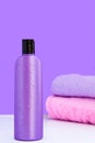 One purple cosmetic bottle and two towels on a lilac background. Spa concept Royalty Free Stock Photo