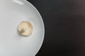 One raw champignon mushroom on a white plate on black table. Not enought food or oversaturation concept. Diet, nutrition