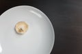 One raw champignon mushroom on a white plate on black table. Not enought food or oversaturation concept. Diet, nutrition