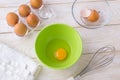 One raw egg in a green bowl, five brown chicken eggs in a transparent plastic tray and  stainless steel whisk on a white wooden Royalty Free Stock Photo