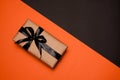 One rectangular gift box wrapped in kraft paper, decorated with a black satin ribbon and bow, lies on an orange-black background Royalty Free Stock Photo