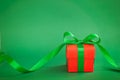 One red christmas gift box with green ribbon on green background Royalty Free Stock Photo