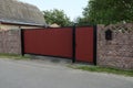 One red metal closed gate and door and part of a brown stone fence