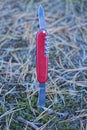 one red open folding knife with gray metal blades sticks out in the ground