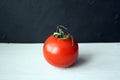 One red tomato with a green sprig on a wooden background