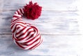 One red and white striped cap with a long tail and a large red pompom is on a white wooden background