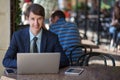 One relaxed young handsome professional businessman working with his laptop, phone and tablet in a noisy cafe.