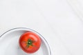 Ripe organic tomato with green stem leaves on white enamel plate on marble stone background. Elegant dishware. Healthy diet