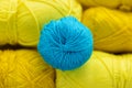 One round ball of blue woolen thread lies on a blurred background of oblong yellow balls on the theme of hand-made knitting or a Royalty Free Stock Photo