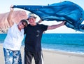 One senior couple of two caucasian people enjoying the beach with the wind. Holding a blue scarf in the sky and smiling. Blue sea Royalty Free Stock Photo