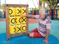 One senior man with white hair plays in the public park with children`s games. Outdoor in a tropical place sitting on the floor