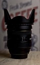 Camera lens standing against a wall with the word `coffee` written and out of focus. Royalty Free Stock Photo