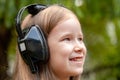 One single happy cheerful school age child, girl wearing large headphones listening to music outdoors, portrait, face closeup Royalty Free Stock Photo