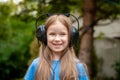 One single happy cheerful school age child, girl wearing large headphones listening to music outdoors, simple portrait, face Royalty Free Stock Photo
