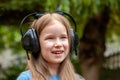 One single happy cheerful school age child, girl wearing large headphones listening to music outdoors, simple portrait, face up Royalty Free Stock Photo