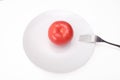 One single red ripe fresh raw tomato on white ceramic plate with a folk isolated on white, mediterranean diet concept Royalty Free Stock Photo