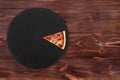 One slices of delicious BBQ pizza with ham, bbq sauce, bacon and salami on a slate black platter which is on wooden table Royalty Free Stock Photo